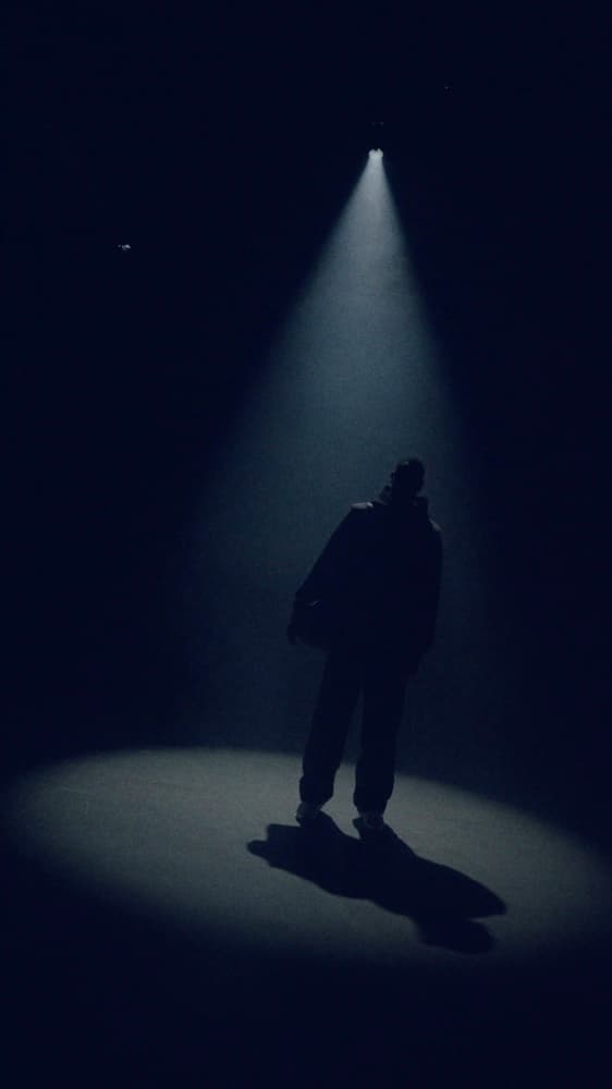 Model moving through a narrow spotlight in the Under Gold Nova campaign film